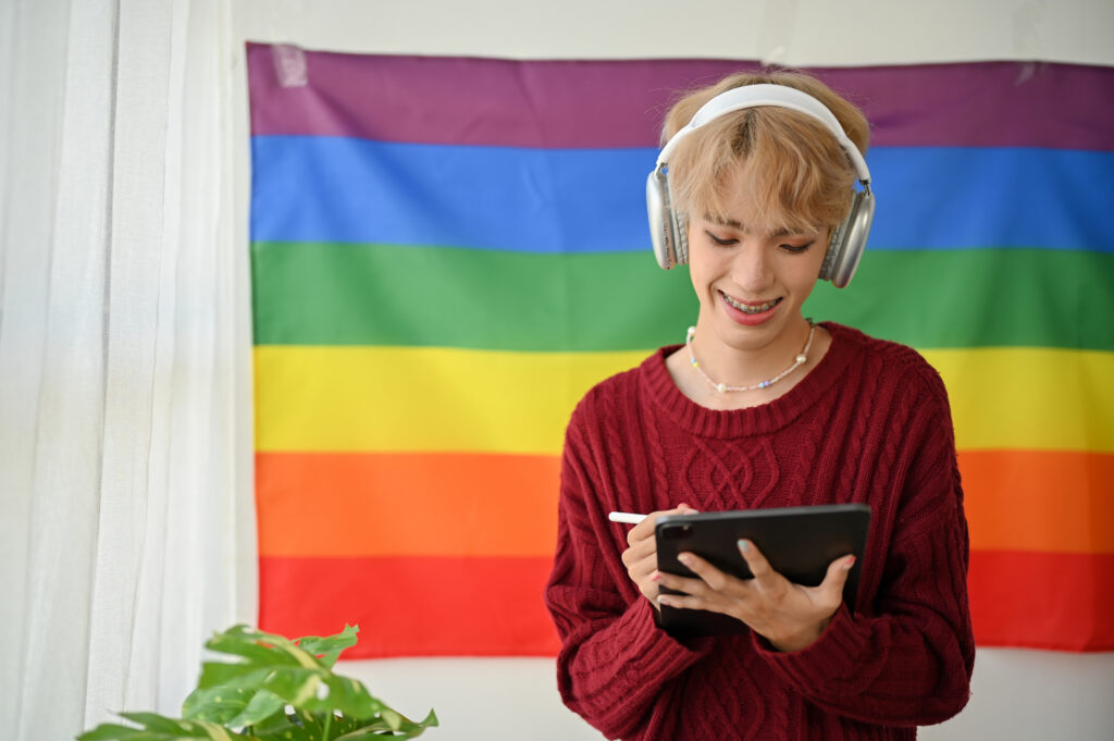 A happy Asian gay man is listening to music and using his tablet while standing in his room