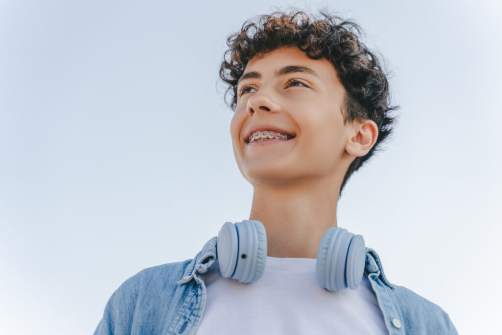 Smiling curly haired teenager with braces wearing headphones looking away standing on the street