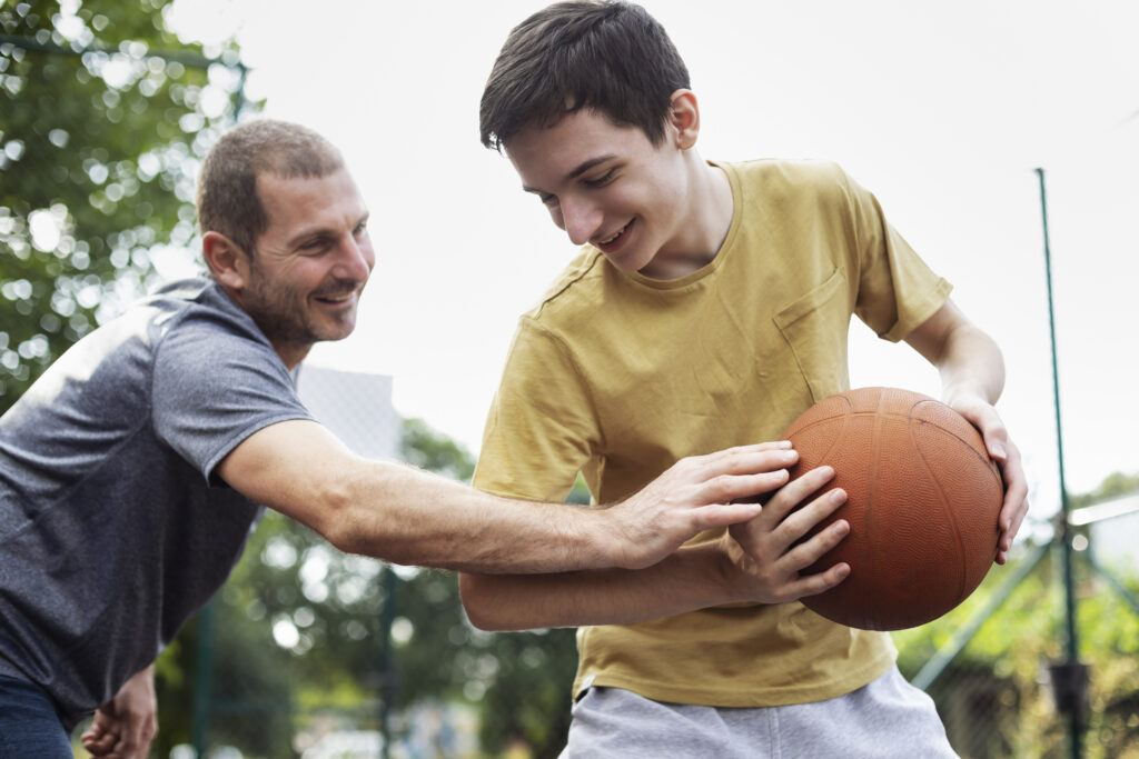 Happy father and son practicing basketball on outdoor court.